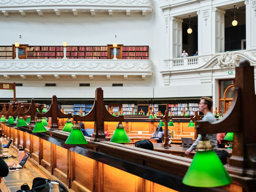 Quiet historical archive reading room with long wooden tables, green lamps and shelves of bound files
