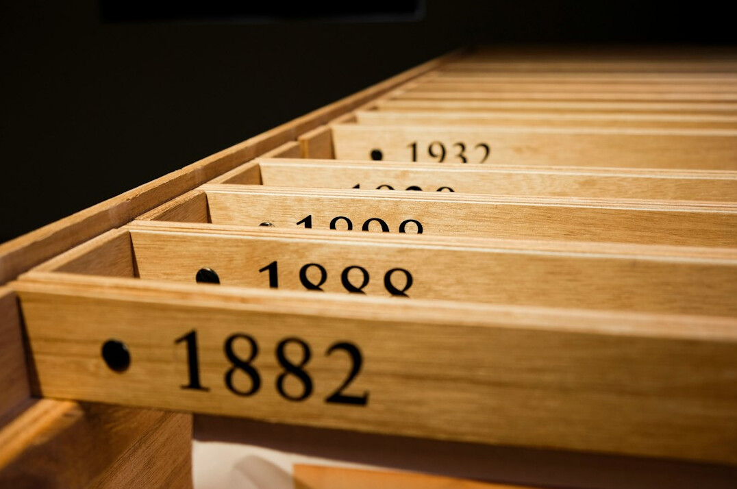 Long archive table with opened historical files, a magnifying glass and an index card box